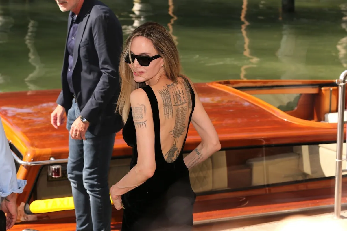 Wearing a black dress, Angelina Jolie stands alongside the river in Venice and offers a closeup of her back tattoos