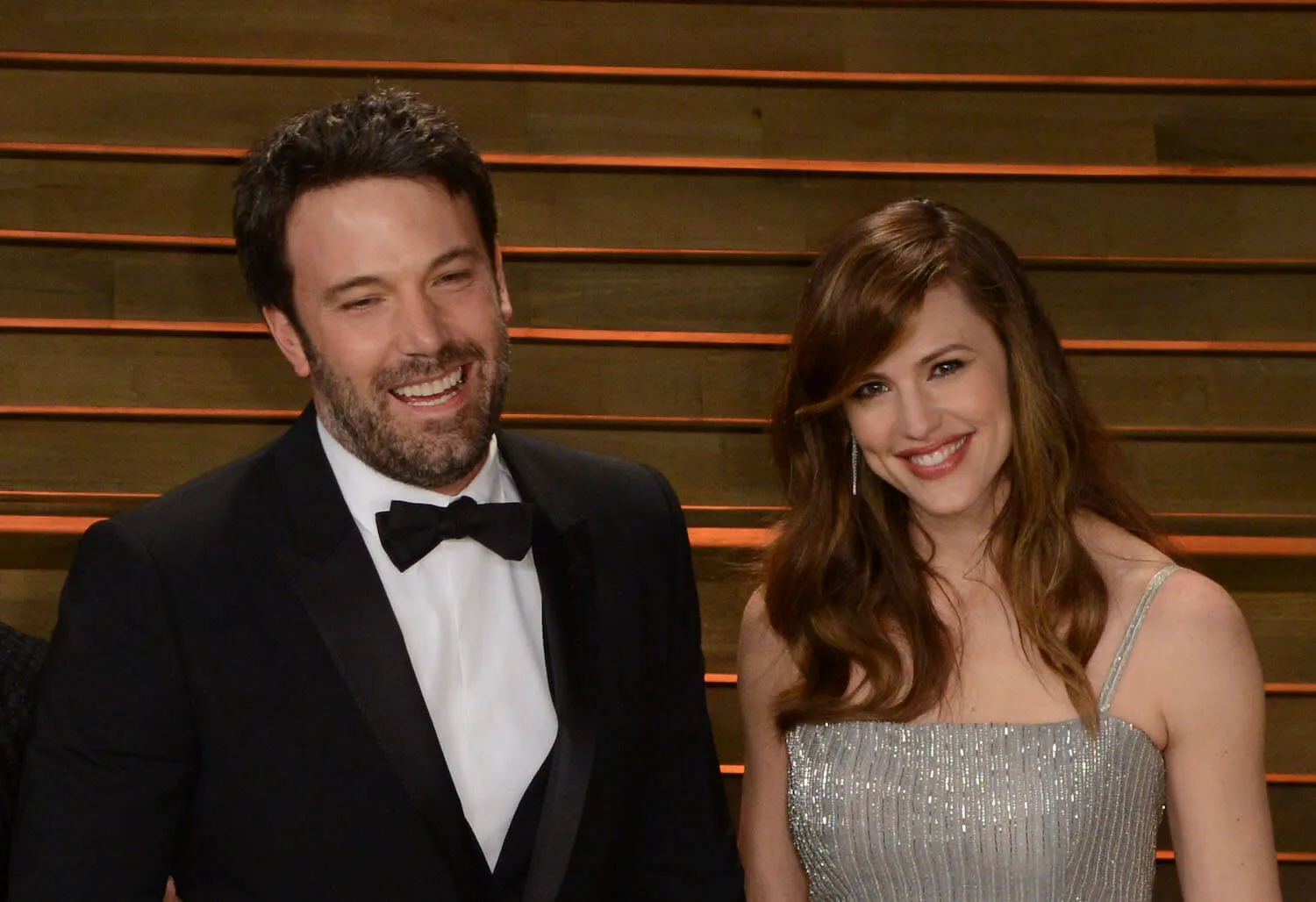 Ben Affleck in a tuxedo and Jennifer Garner in a dress smiling while standing next to each other at the Vanity Fair Oscar Party in 2014