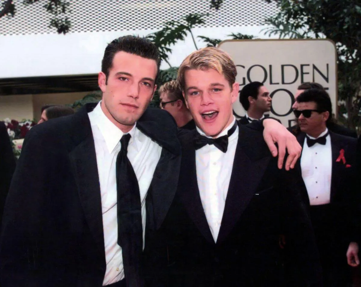 Ben Affleck stands with his arm around Matt Damon's shoulders at the Golden Globes. They both wear suits.