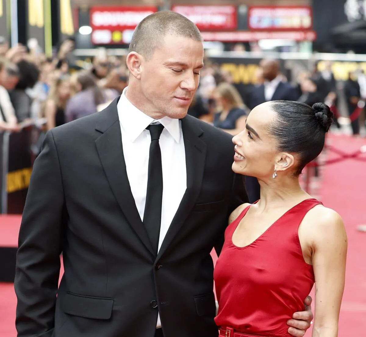 Channing Tatum and Zoe Kravitz stand together on a red carpet. He wears a suit and she wears a red dress.