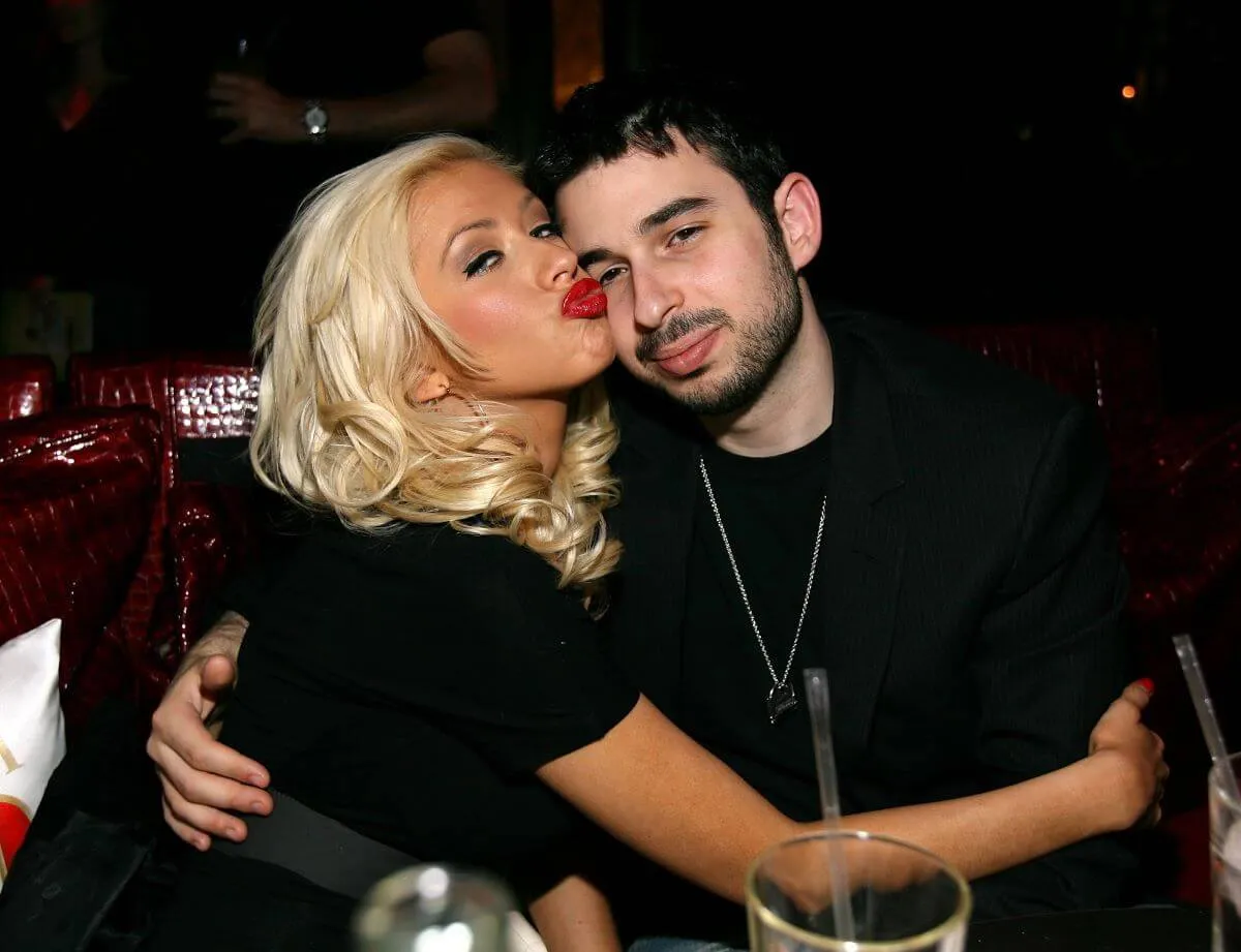 Christina Aguilera kisses the side of Jordan Bratman's head and wraps her arms around him. They both wear black.