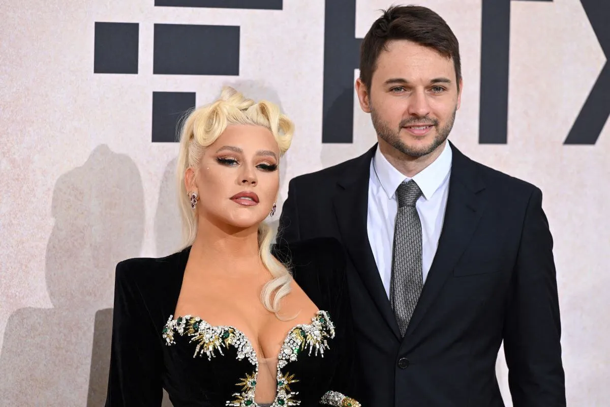 Christina Aguilera and Matthew Rutler stand together. She wears a black dress and he wears a suit.