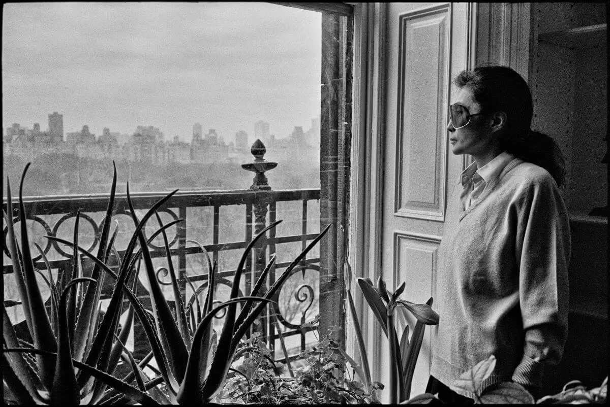 A black and white picture of Yoko Ono wearing sunglasses and looking out the window.