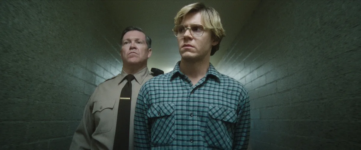 Evan Peters as Jeffrey Dahmer walking down a hallway with a police man behind him in Netflix's 'Monster: The Jeffrey Dahmer Story'