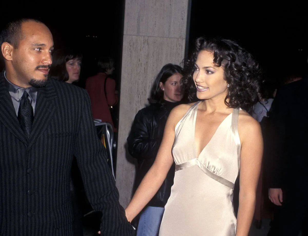 David Cruz and Jennifer Lopez hold hands at a movie premiere. He wears a suit and she wears a white dress.