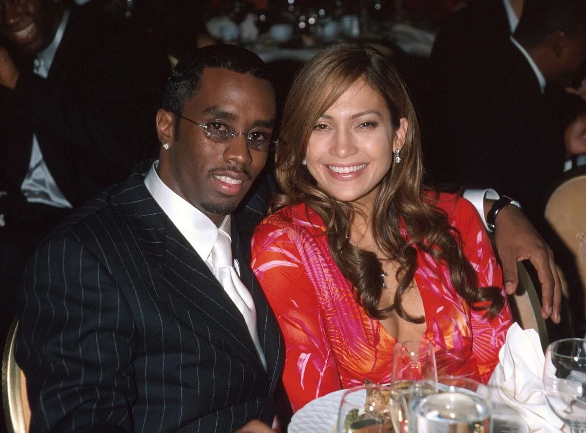 Sean "Diddy" Combs wears a suit and sits with his arm around Jennifer Lopez, who wears a magenta dress.