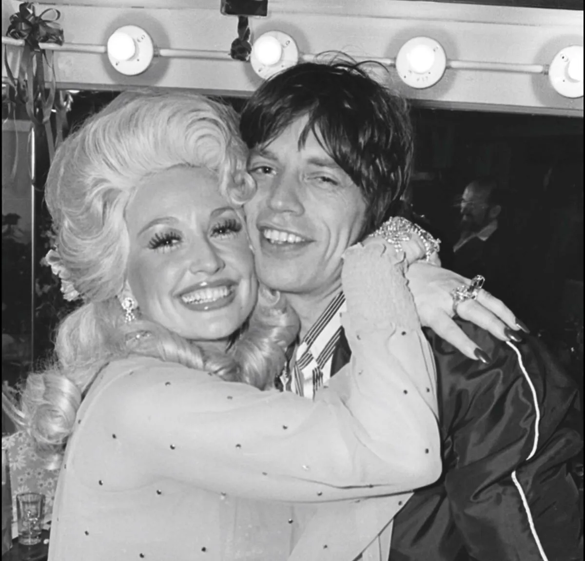 A black and white picture of Dolly Parton hugging Mick Jagger in 1977.