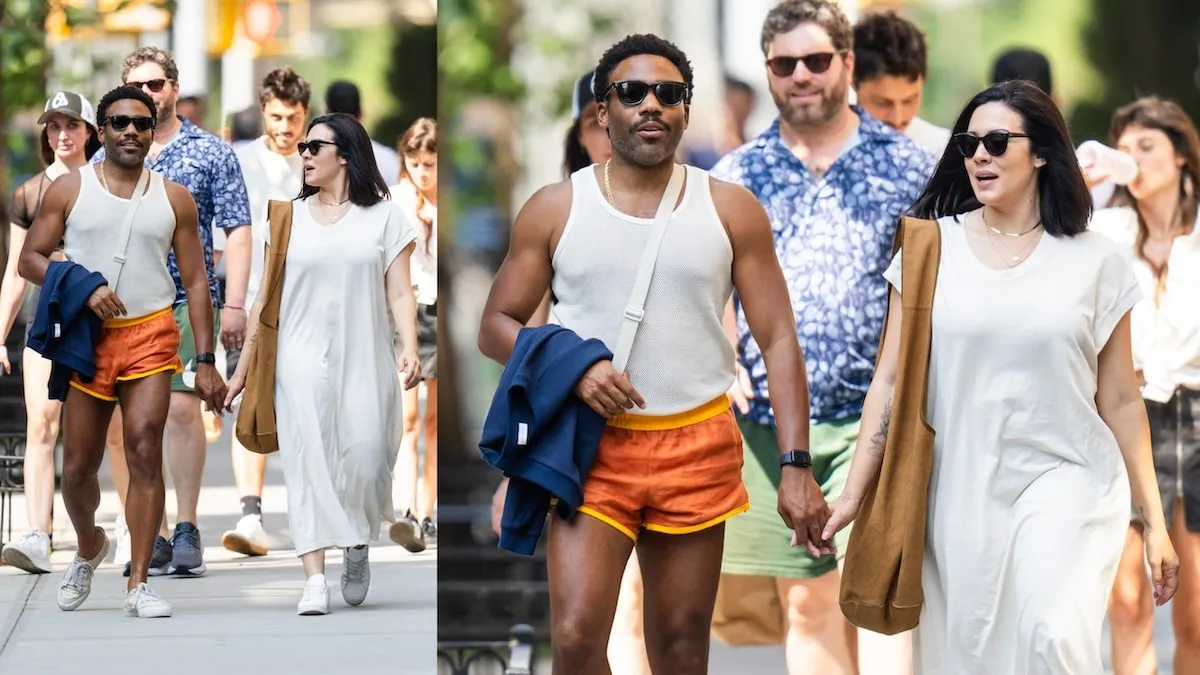 Wearing a white tank top and orange shorts, Donald Glover walks down an NYC street holding hands with his wife Michelle White, wearing a white dress