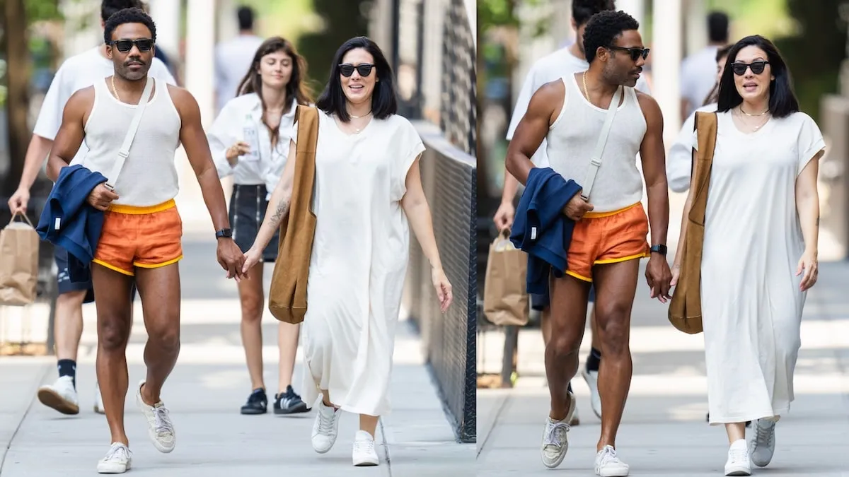 Wearing a white tank top and orange shorts, Donald Glover walks down an NYC street holding hands with his wife Michelle White, wearing a white dress