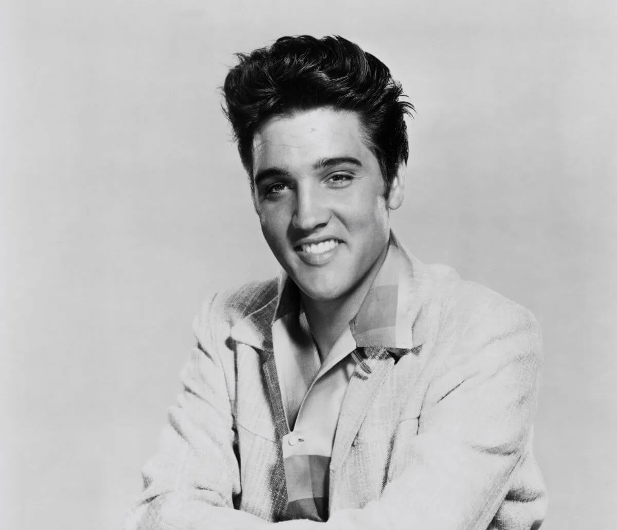 A black and white picture of Elvis Presley wearing a jacket and smiling.