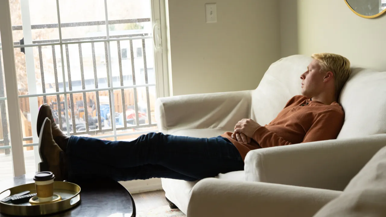 Ethan Plath of 'Welcome to Plathville' sitting on a couch with his feet on the coffee table and looking out the window