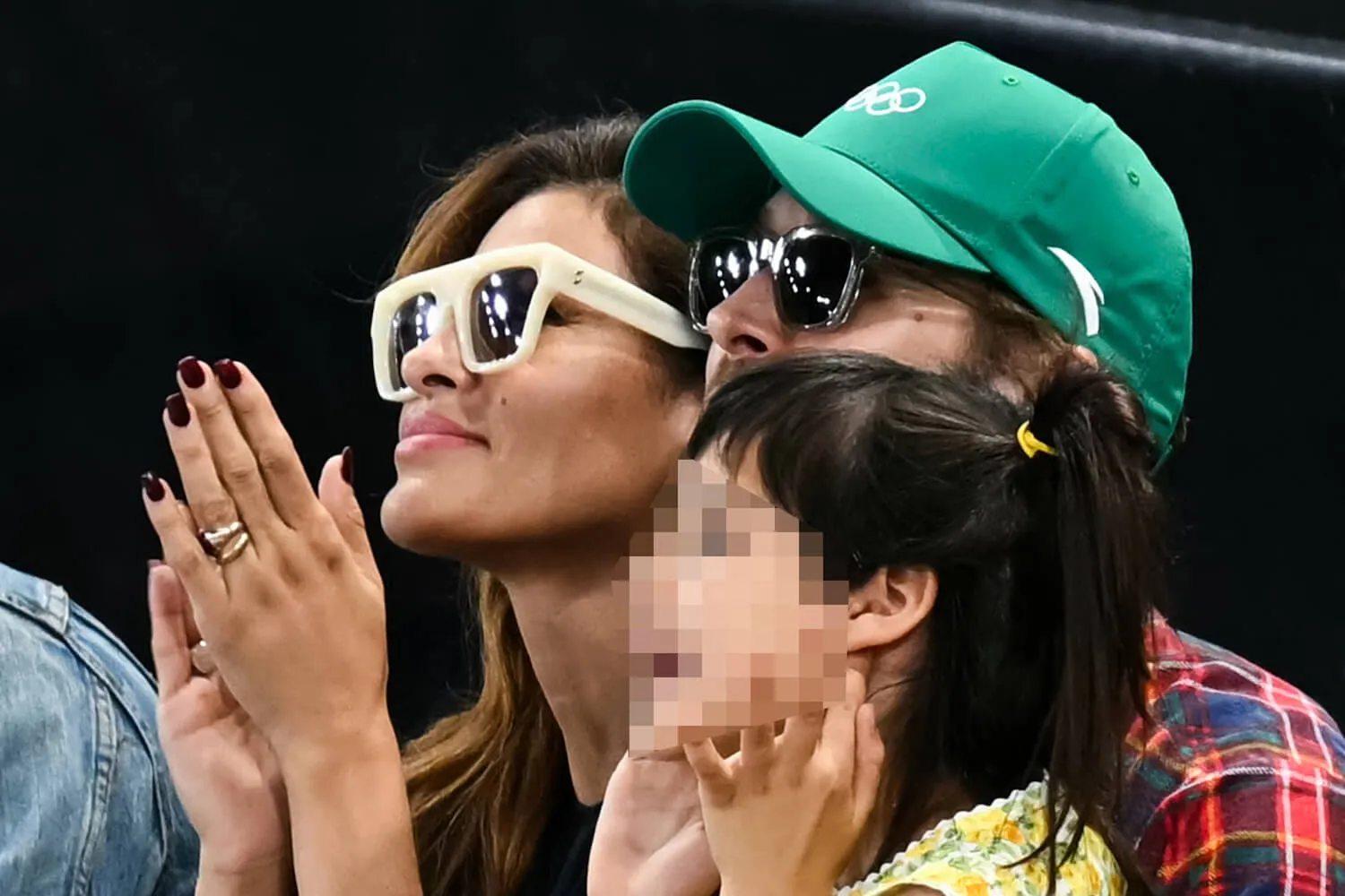 A close-up of Eva Mendes and Ryan Gosling at the Olympics with one of their daughters, whose face is blurred out.