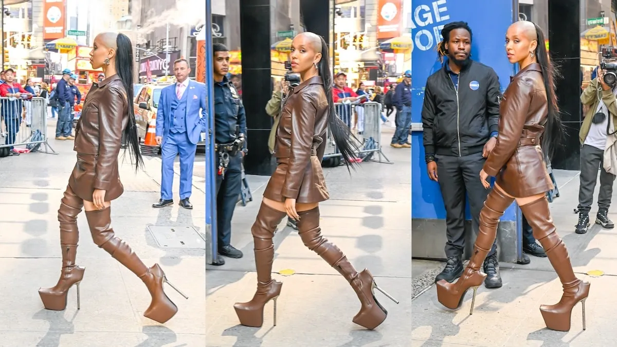 Singer FKA twigs walks past fans on an NYC street while wearing a brown leather outfit and shaved head hairstyle