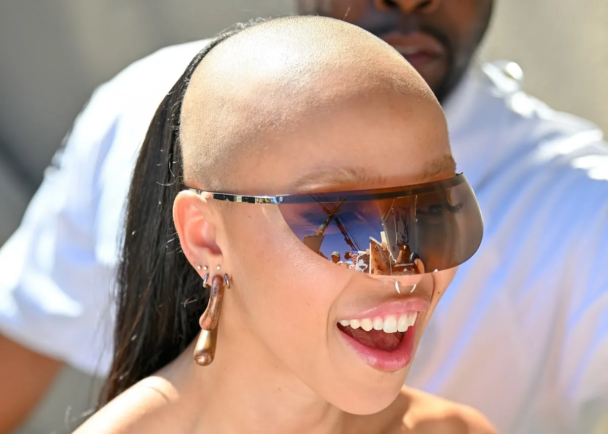 Singer FKA twigs smiles for paparazzi with a shaved head and futuristic sunglasses