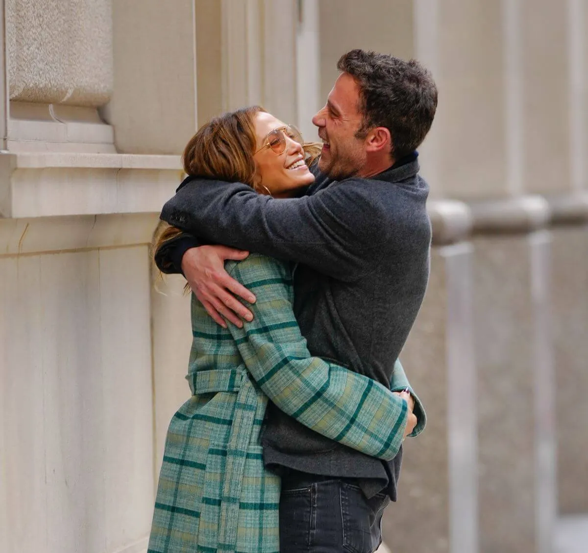 Jennifer Lopez wears a green coat and sunglasses and hugs Ben Affleck, who wears a gray jacket.