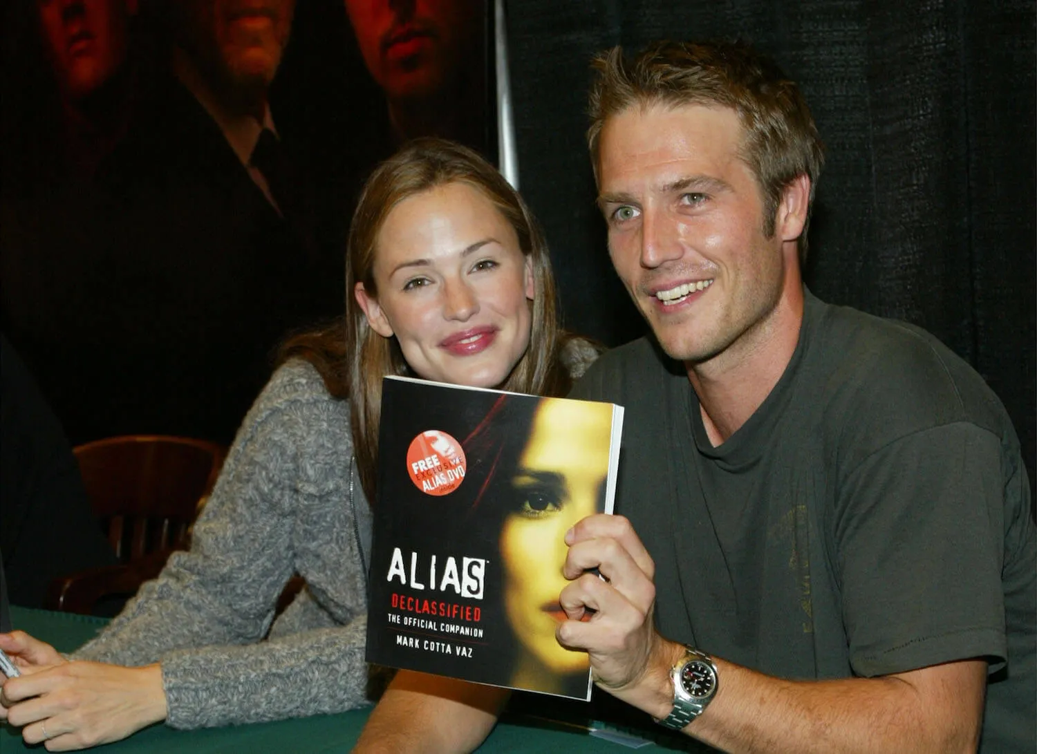 Jennifer Garner and Michael Vartan sitting next to each other and holding an 'Alias' book at the 'Alias Declassified: The Official Companion' book signing event in 2002