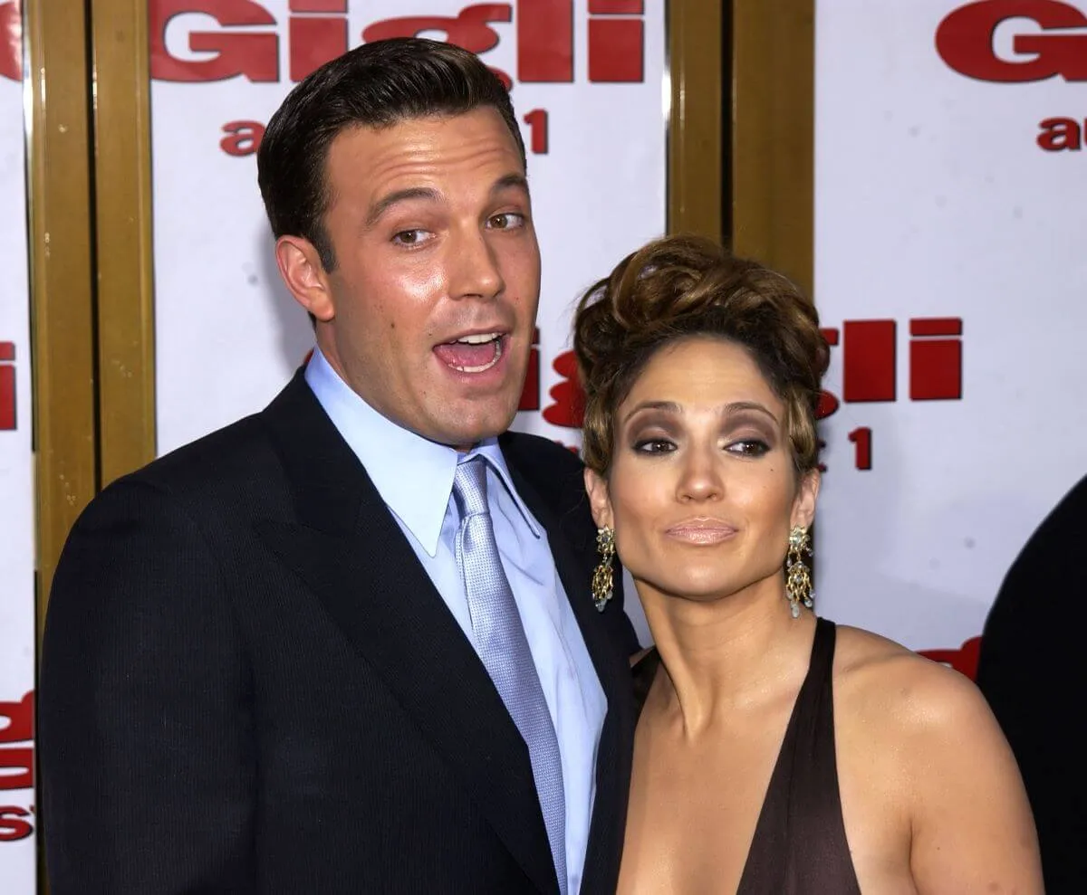 Ben Affleck and Jennifer Lopez pose together at the 'Gigli' premiere. He wears a suit and she wears a black dress.