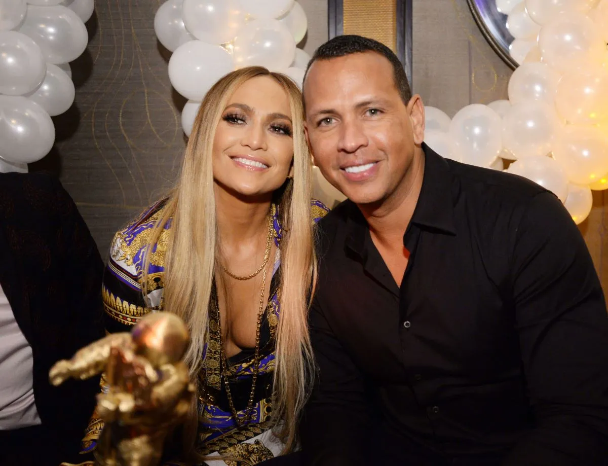 Jennifer Lopez and Alex Rodriguez sit together. She wears a patterned shirt and gold necklace and he wears a black shirt.