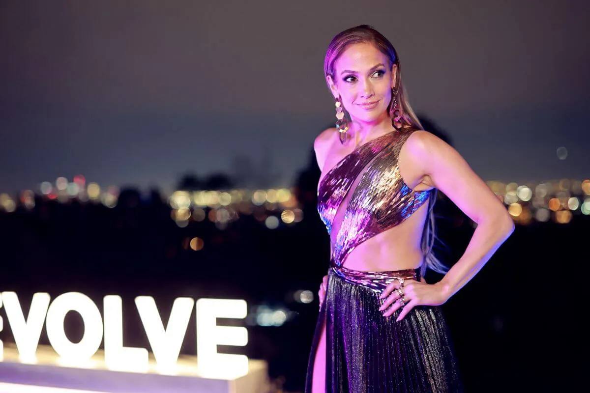 Jennifer Lopez wears a metallic dress and stands with her hand on her hip.