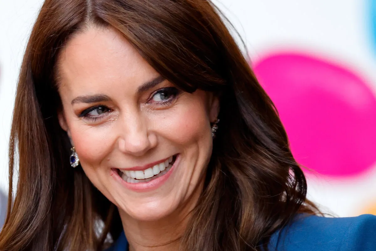 Kate Middleton, who isn't a Stepford wife but a role model, per an author, smiles wearing blue.