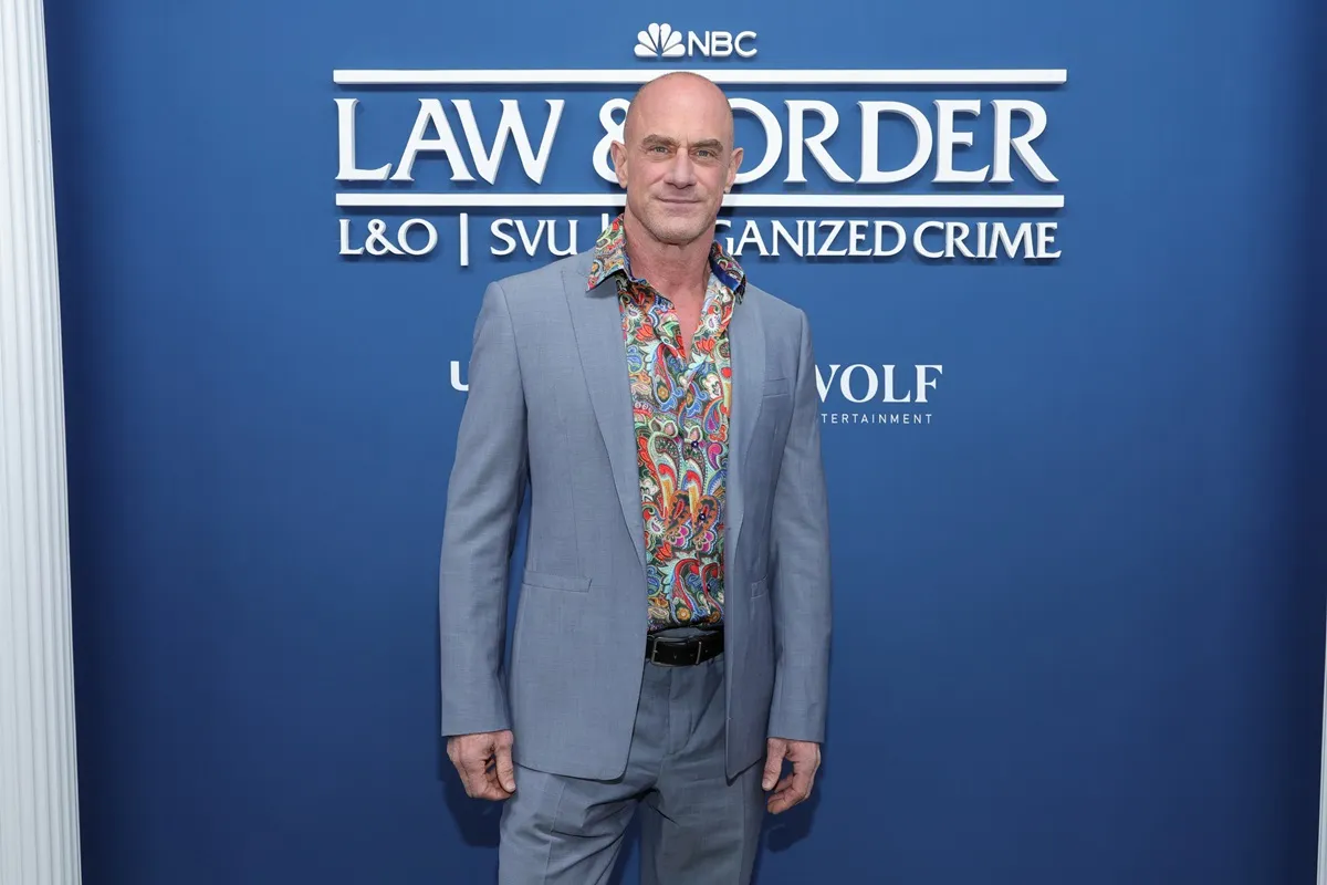 Chris Meloni posing in a blue suit in front of a 'Law & Order' poster.