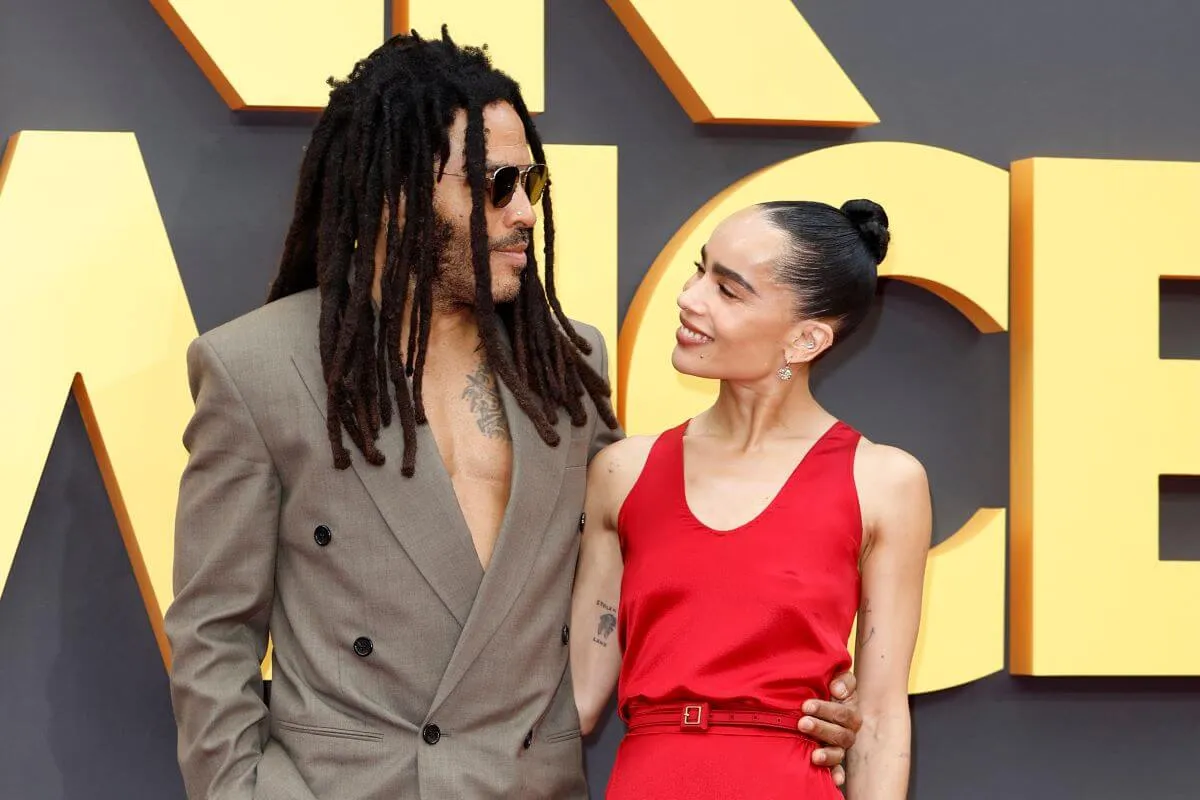 Lenny and Zoe Kravitz stand with their arms around each other. He wears a tan suit and sunglasses and she wears a red dress.