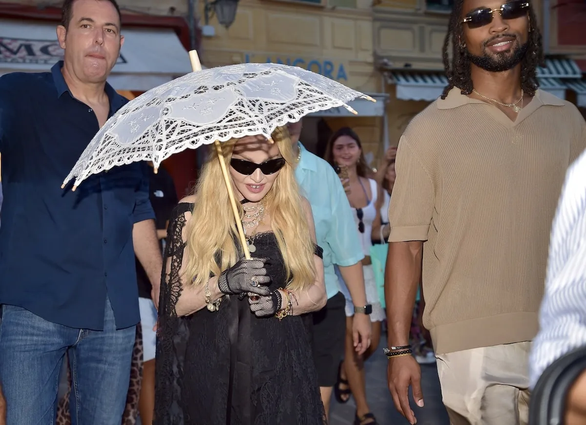 Wearing a black dress and carrying a white lacy umbrella, Madonna walks through Portofino, Italy, with her boyfriend Akeem Morris