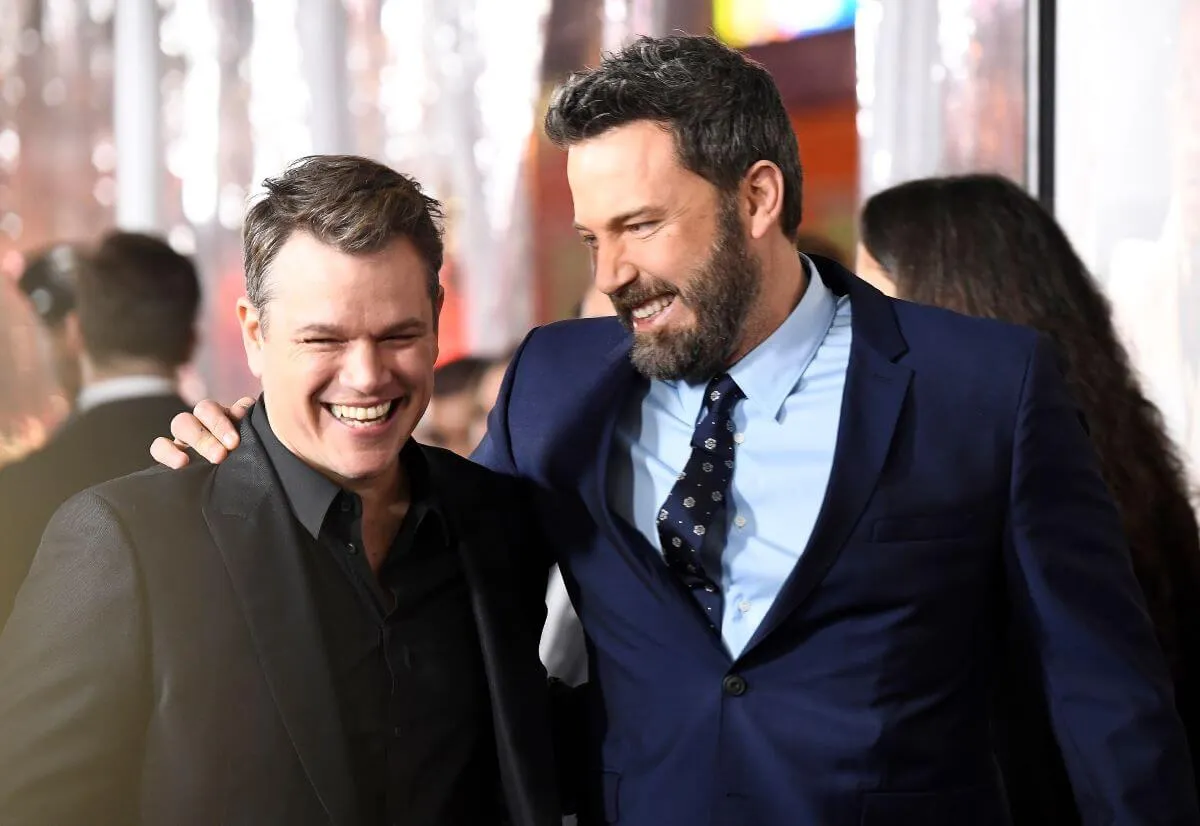 Matt Damon and Ben Affleck stand with their arms around each other.