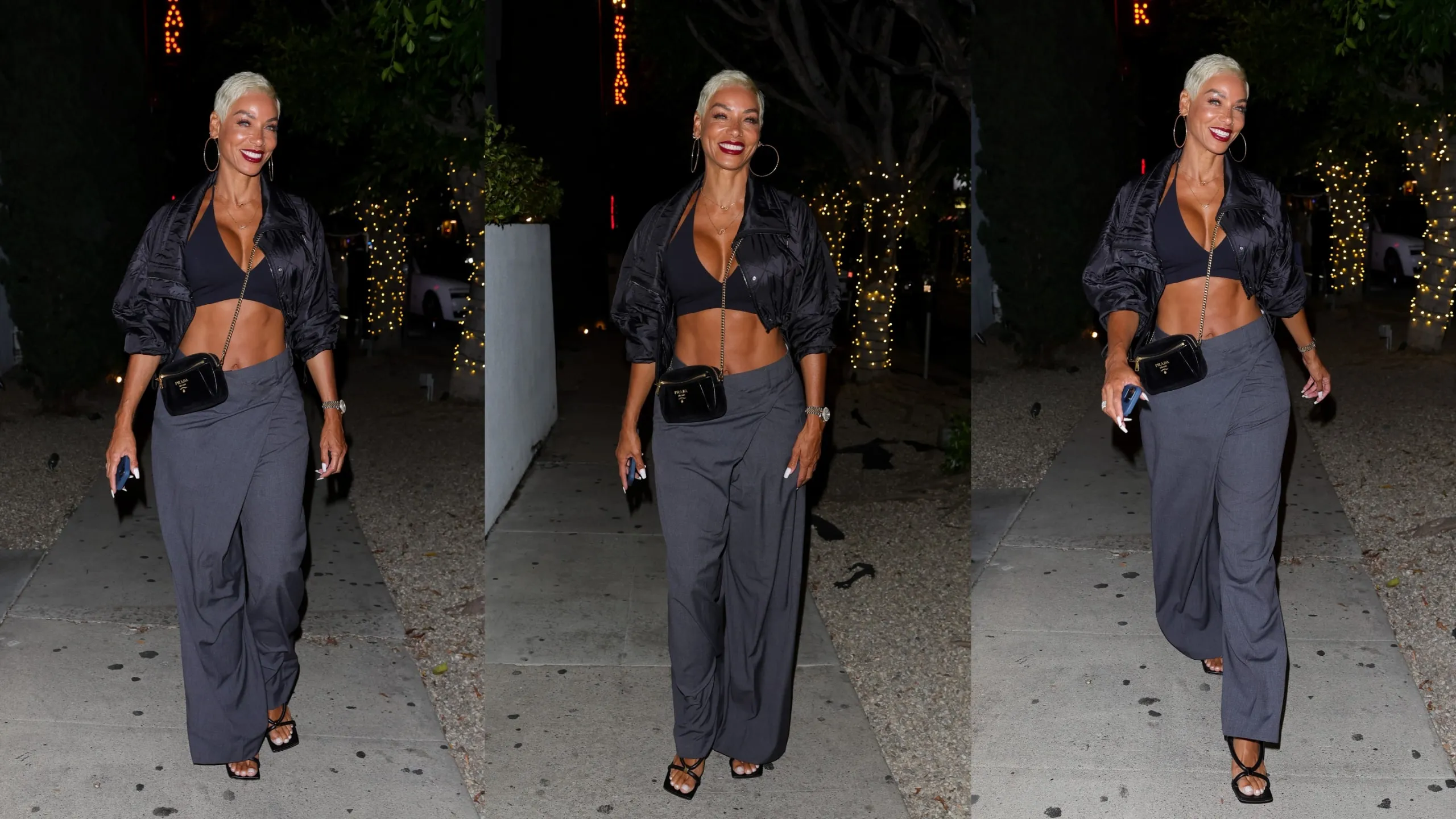 Wearing a black coat and pants, Nicole Murphy smiles for paparazzi outside of a steakhouse in LA