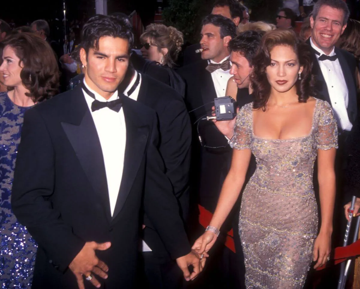 Jennifer Lopez and her husband Ojani Noa hold hands on the red carpet. She wears a silver dress and he wears a tuxedo.