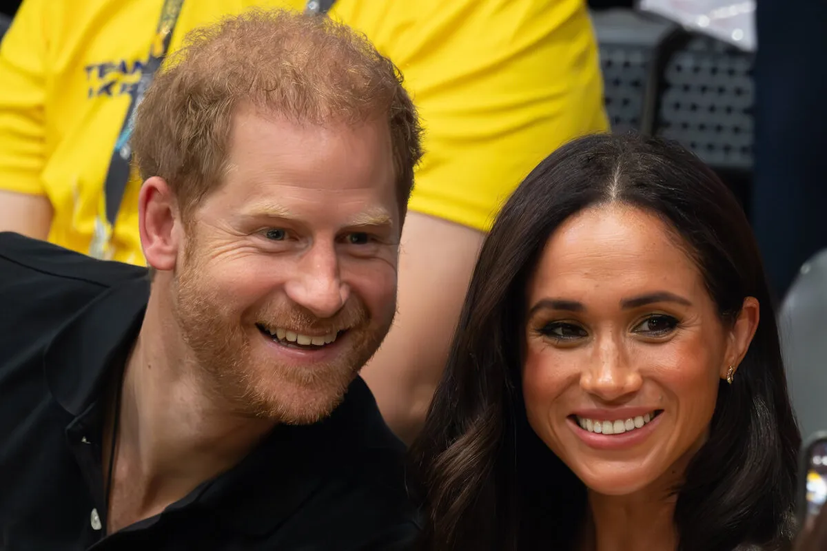 Prince Harry and Meghan Markle, who wants Prince Harry to be done with his lawsuits, smile sitting next to each other.