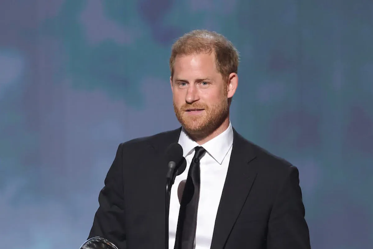 Prince Harry, who has to follows rules before visiting the U.K. as part of his current security situation, speaks into a microphone.