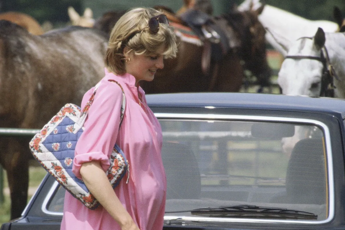 Princess Diana carries one of her iconic fashion items, a handbag, while wearing a pink dress.