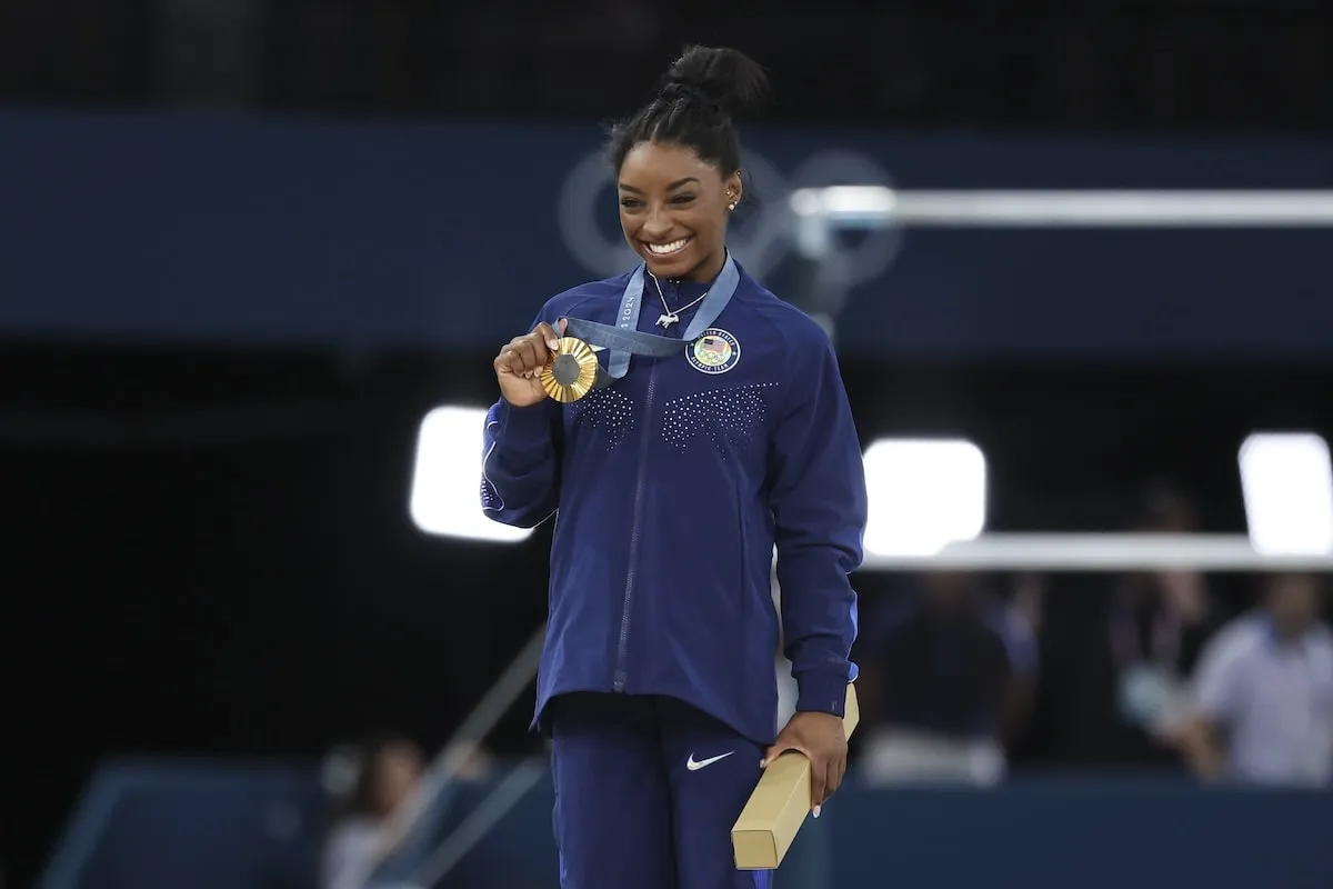 Gymnast Simone Biles smiles and holds up her gold medal after winning the Women's All-Around