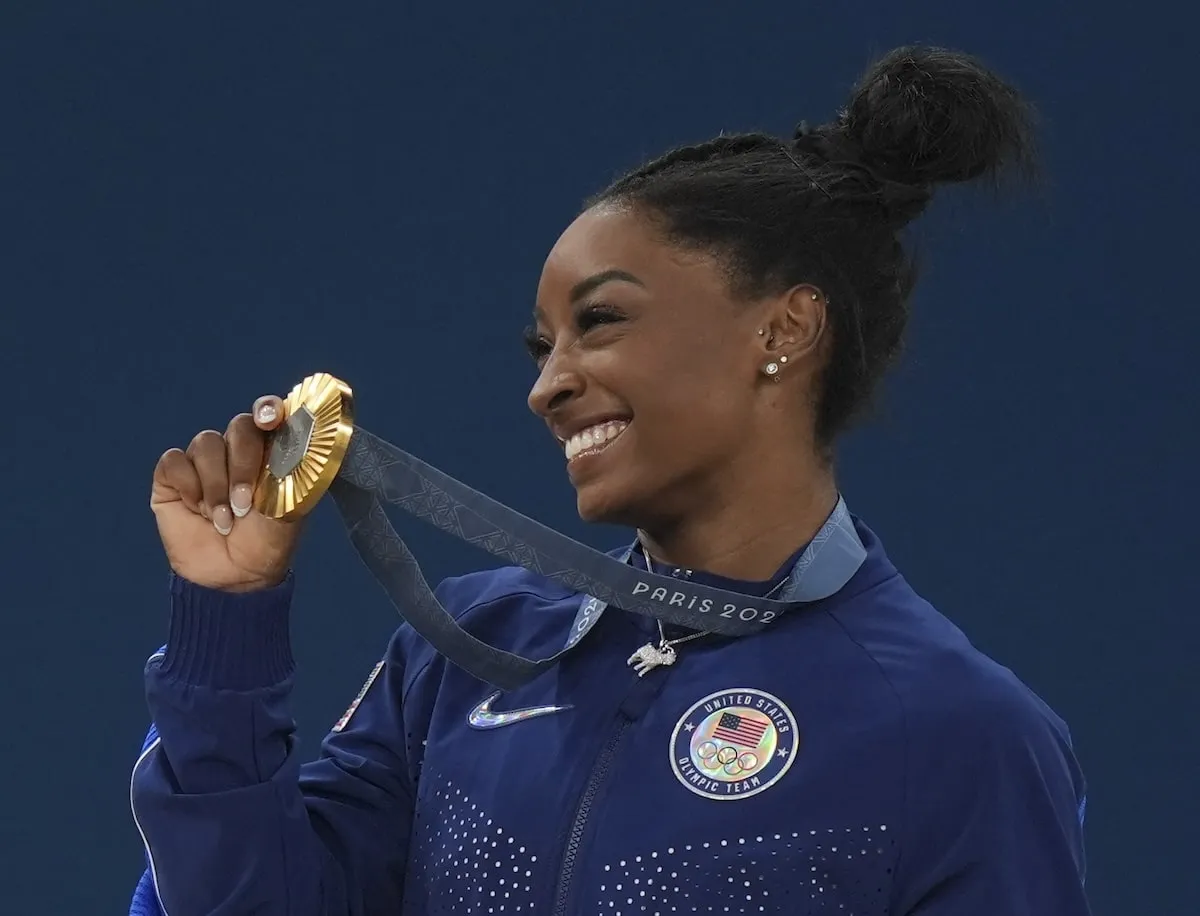 Olympic gymnast Simone Biles smiles for cameras while holding up her gold medal