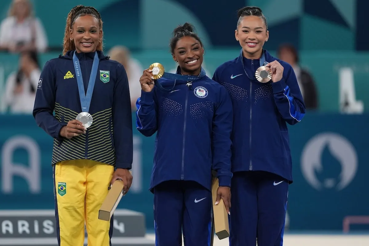 The silver, gold, and bronze medalists, Rebeca Andrade, Simone Biles, and Sunisa Lee, smile for cameras while holding up their medals