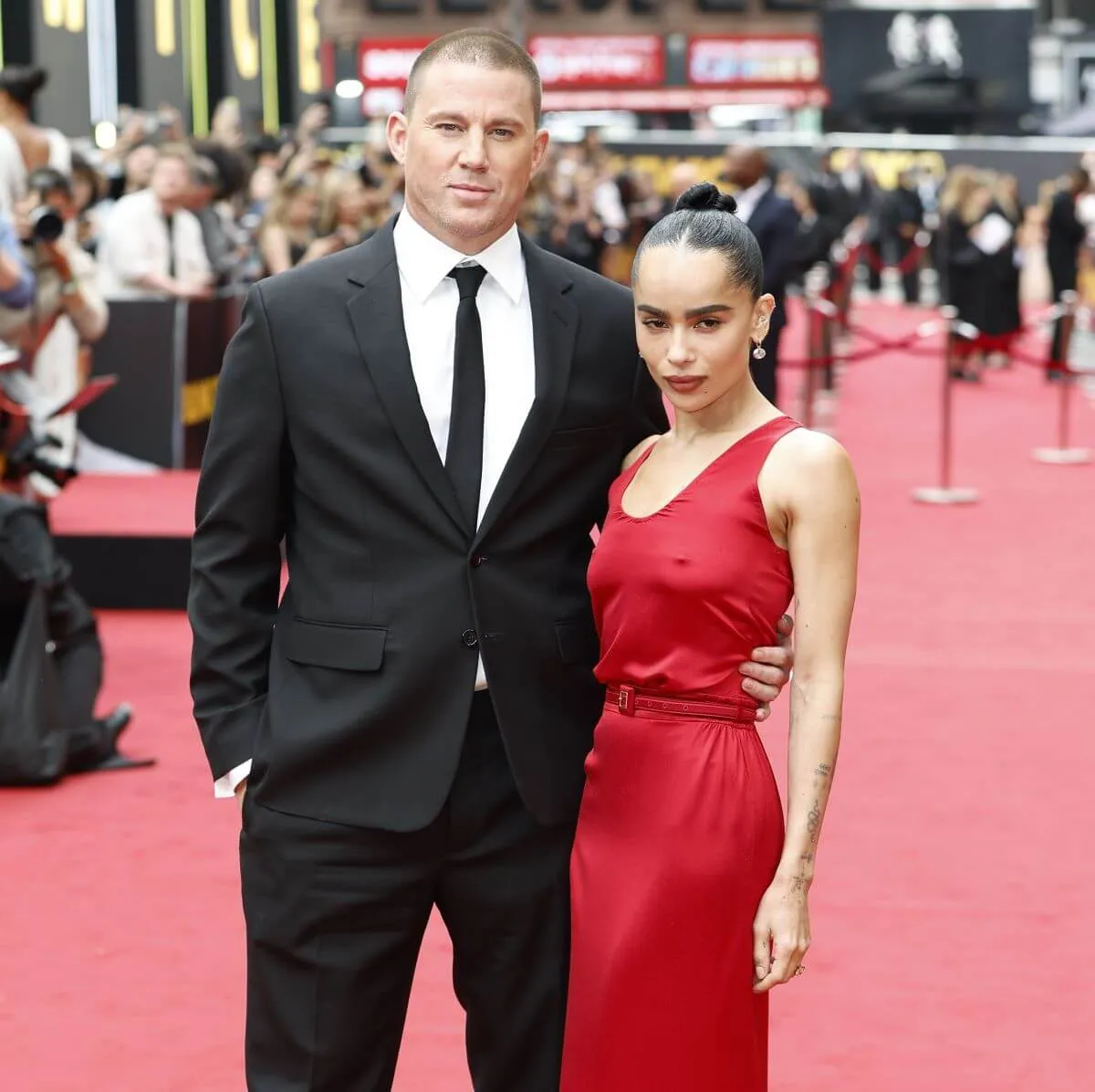 Channing Tatum and Zoe Kravitz stand with their arms around each other on the red carpet. He wears a suit and she wears a red dress.