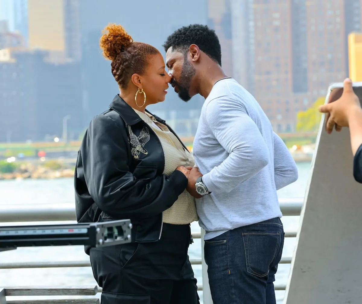 Tory Kittles and Queen Latifah kiss while filming a scene for The Equalizer on Long Island City, Queens, with the NYC skyline behind them