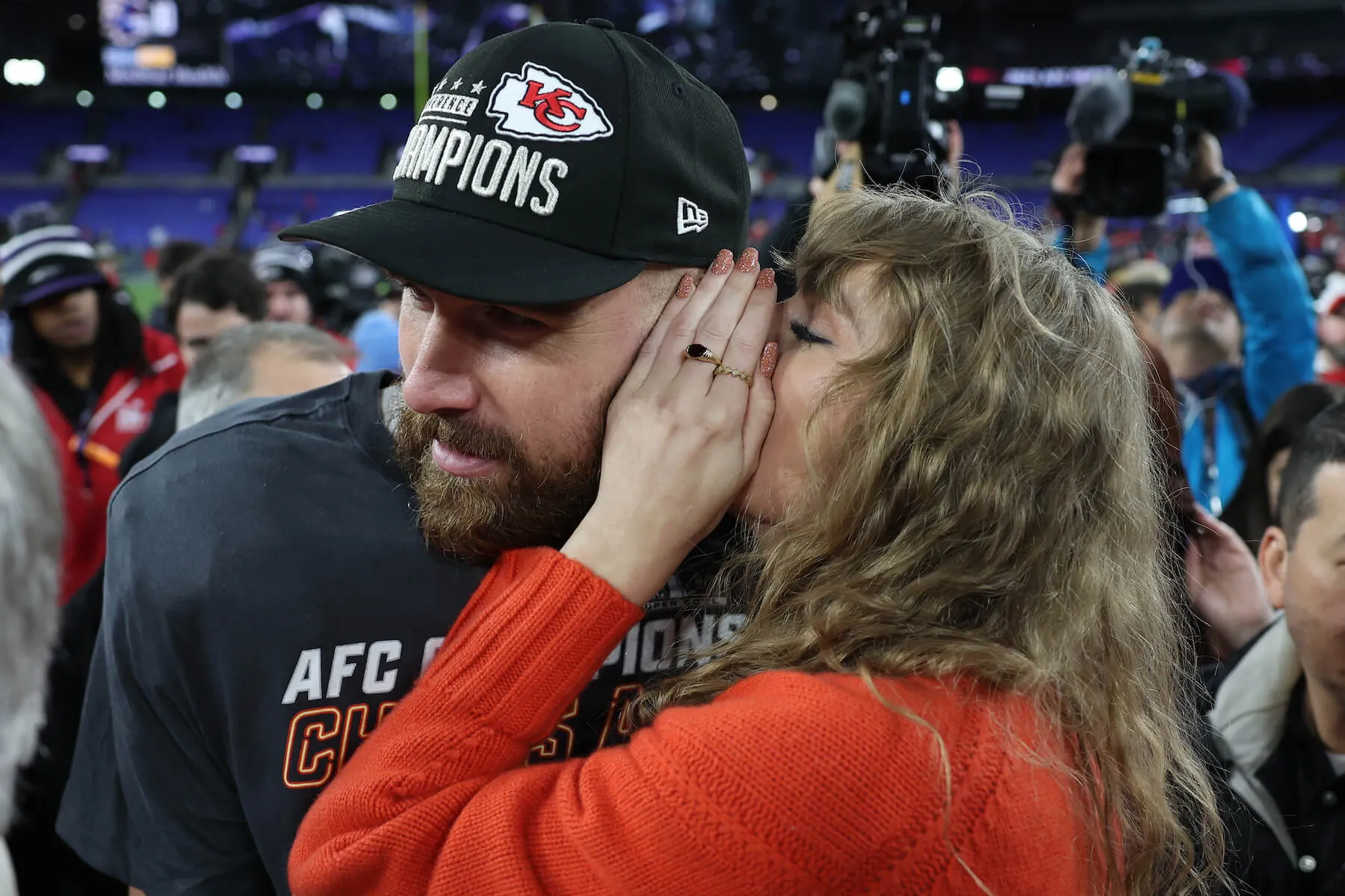 A close-up of Taylor Swift whispering into Travis Kelce's ear