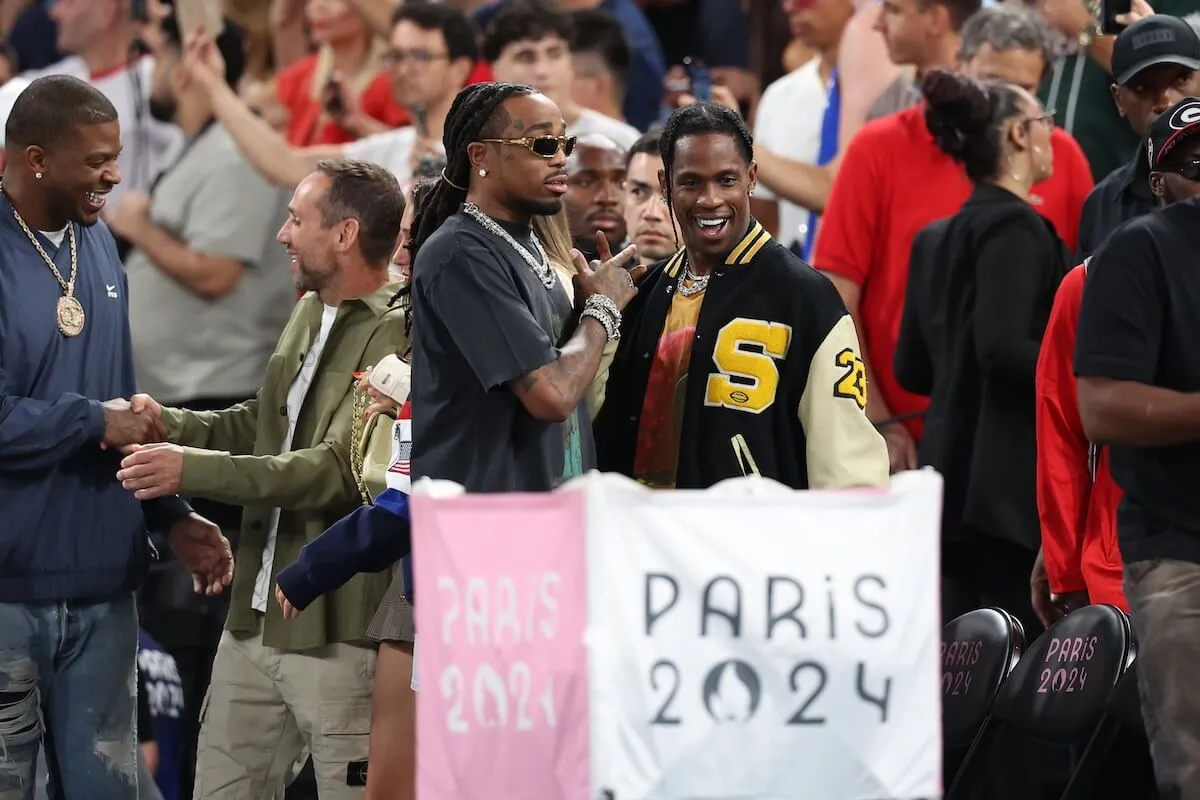 Quavo and Travis Scott standing behind a Paris 2024 banner