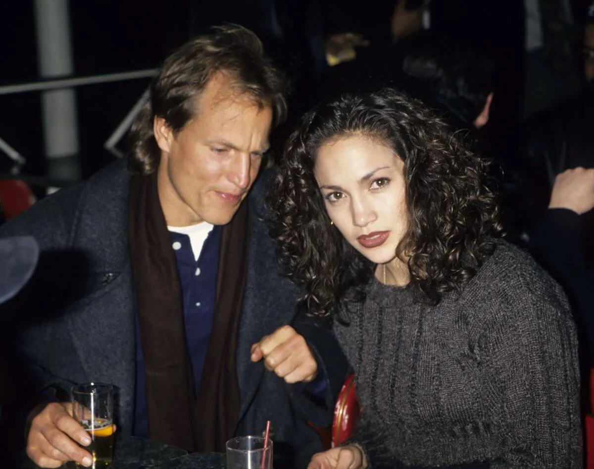 Woody Harrelson and Jennifer Lopez sit together. He holds a glass.