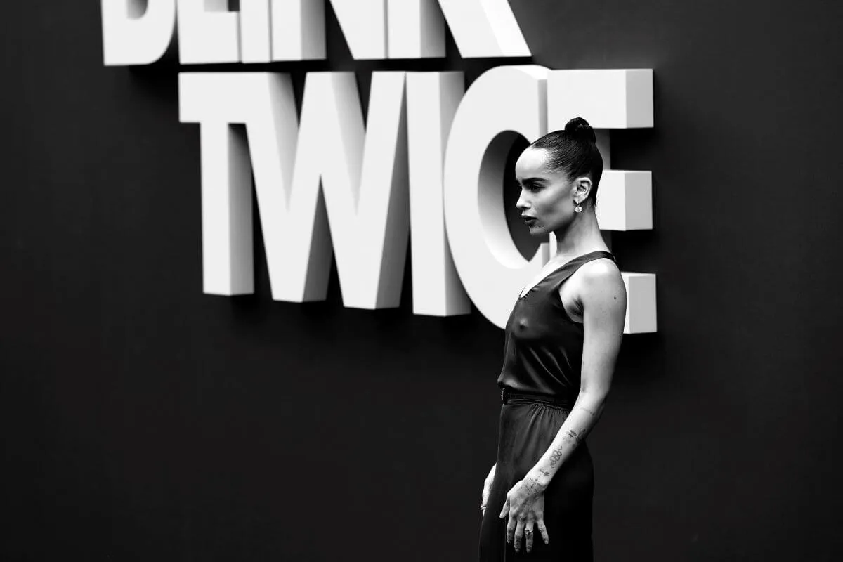 A black and white picture of Zoe Kravitz standing in front of signage for 'Blink Twice.'