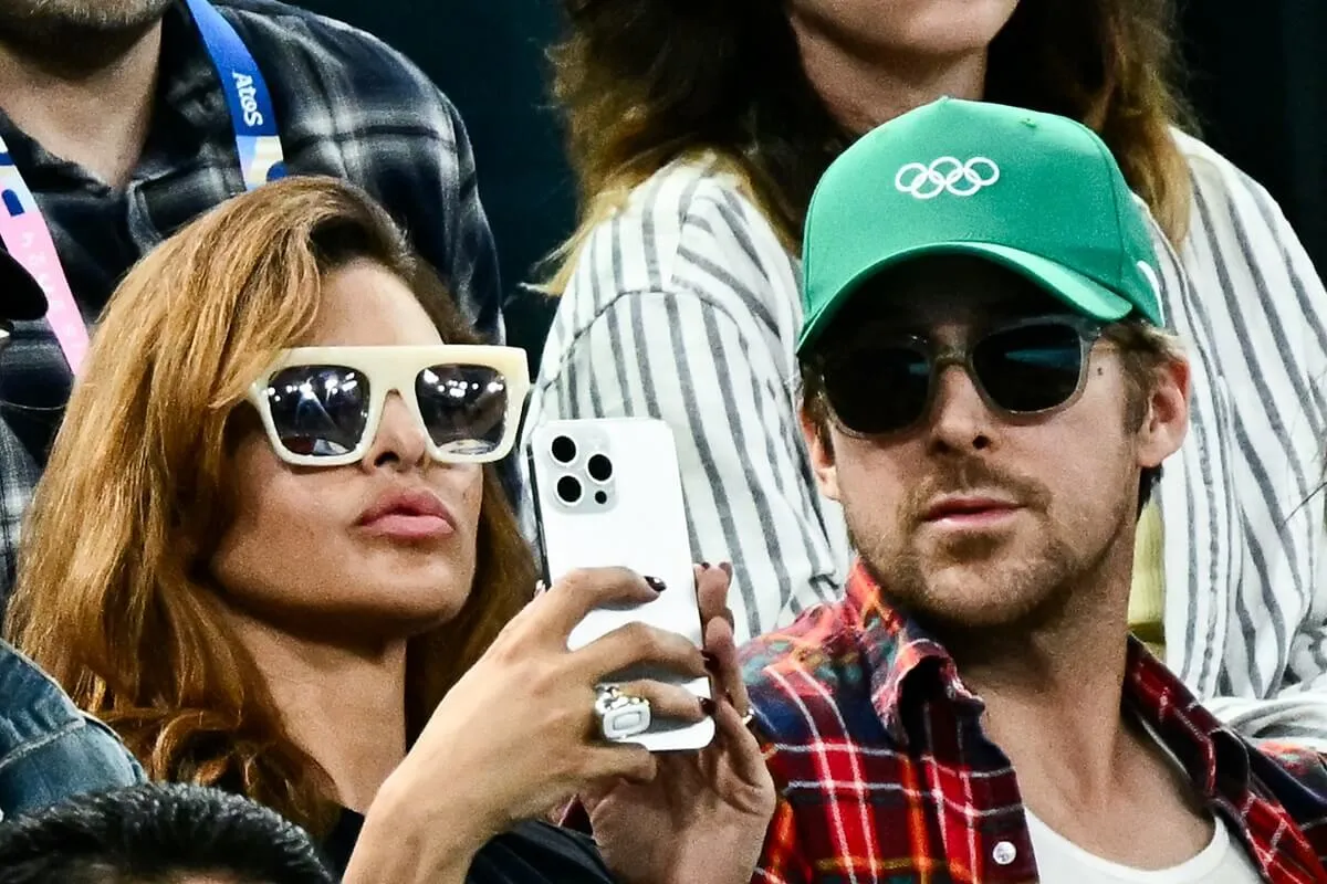 Eva Mendes sitting next to Ryan Gosling while taking a picture on her phone.
