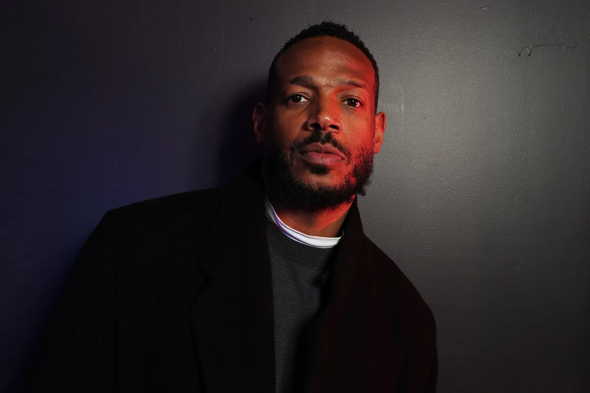 Marlon Wayans posing at the Apollo theater in a black jacket and shirt.