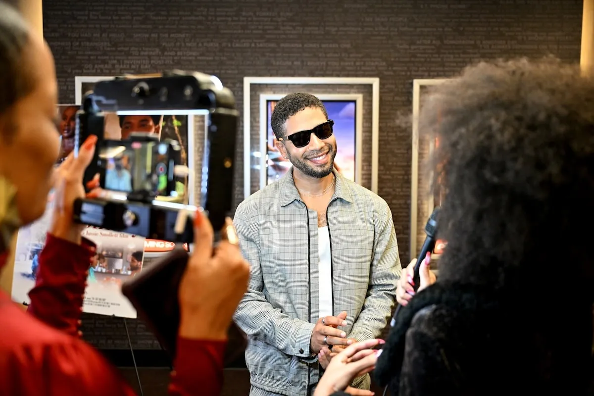 Wearing a plaid jacket and pants, Jussie Smollett speaks to reporters at the Atlanta premiere of "The Lost Holliday"