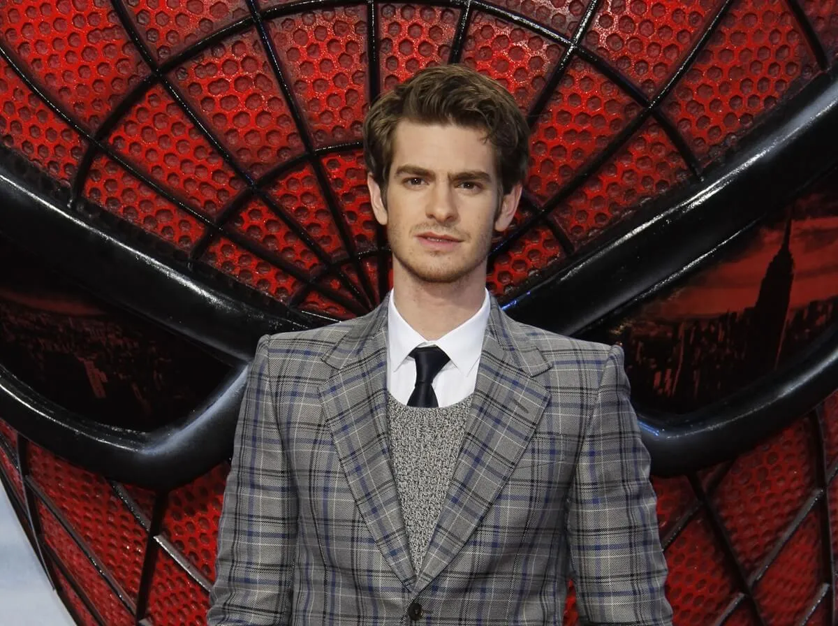 Andrew Garfield posing in front of a Spider-Man poster.