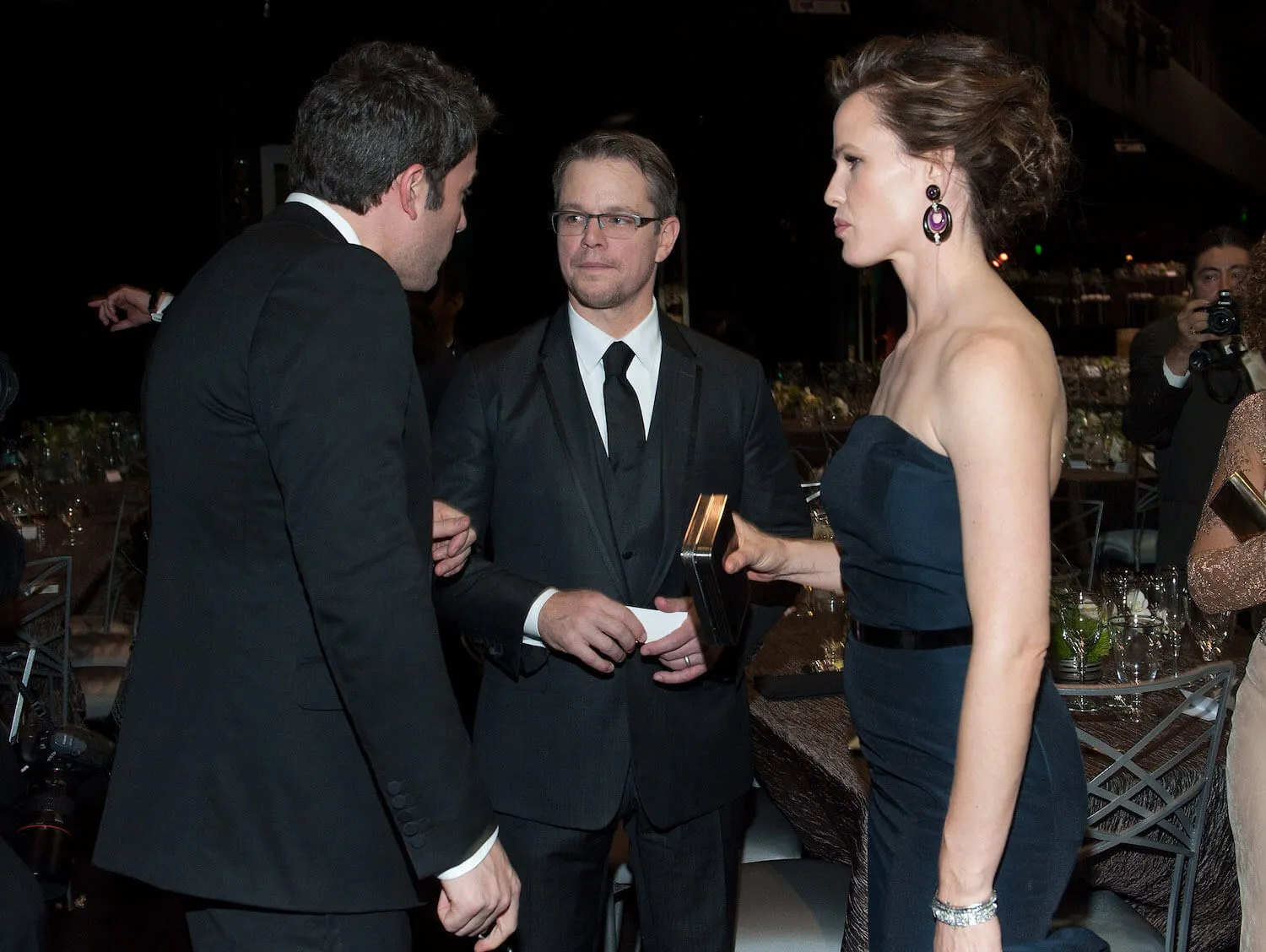 Ben Affleck, Matt Damon, and Jennifer Garner standing in a circle and talking at the Screen Actors Guild Awards in 2014. Affleck and Damon are in suits and Garner is wearing a strapless gown.