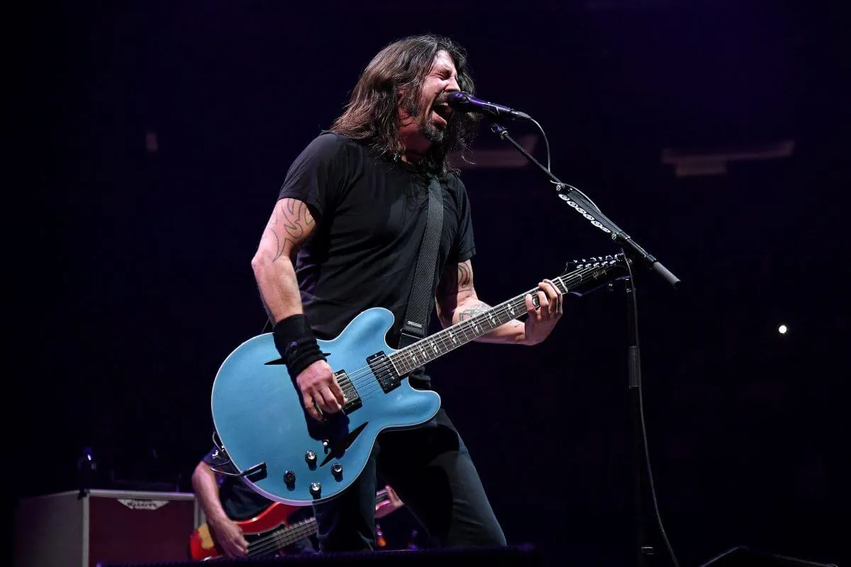 Dave Grohl plays a blue guitar and signs into a microphone.