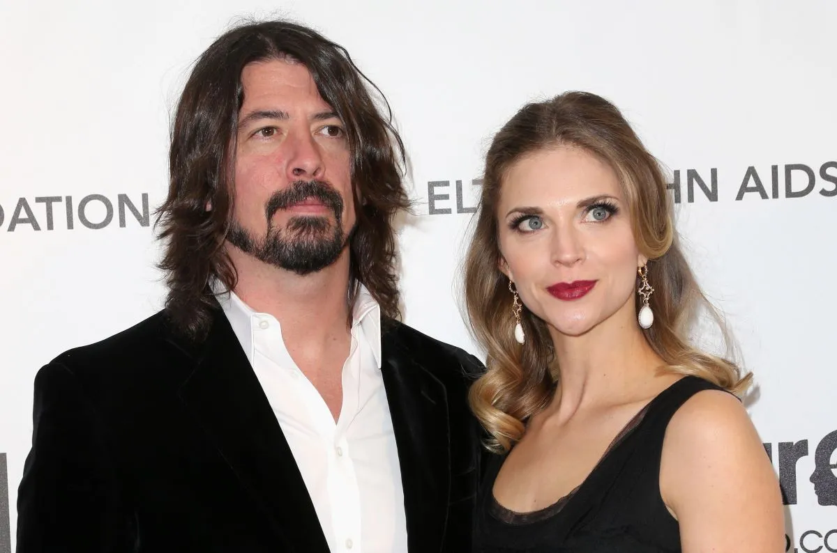 Dave Grohl and his wife Jordyn Blum wear black and stand against a white background.