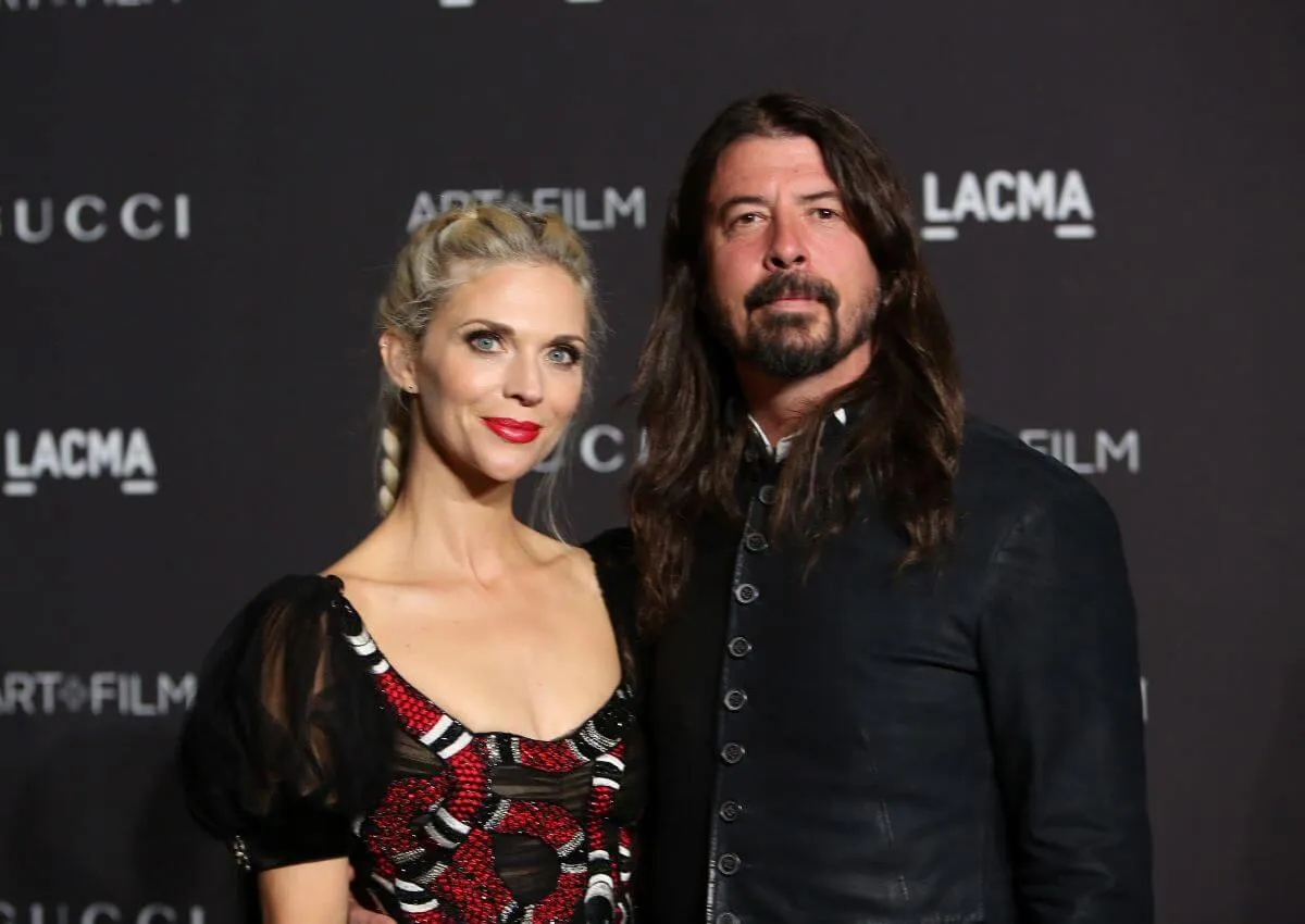 Dave Grohl and his wife, Jordyn Blum stand together at an event for LACMA. He wears a black shirt and she wears a red dress.